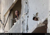 A man and a girl look out from a damaged building